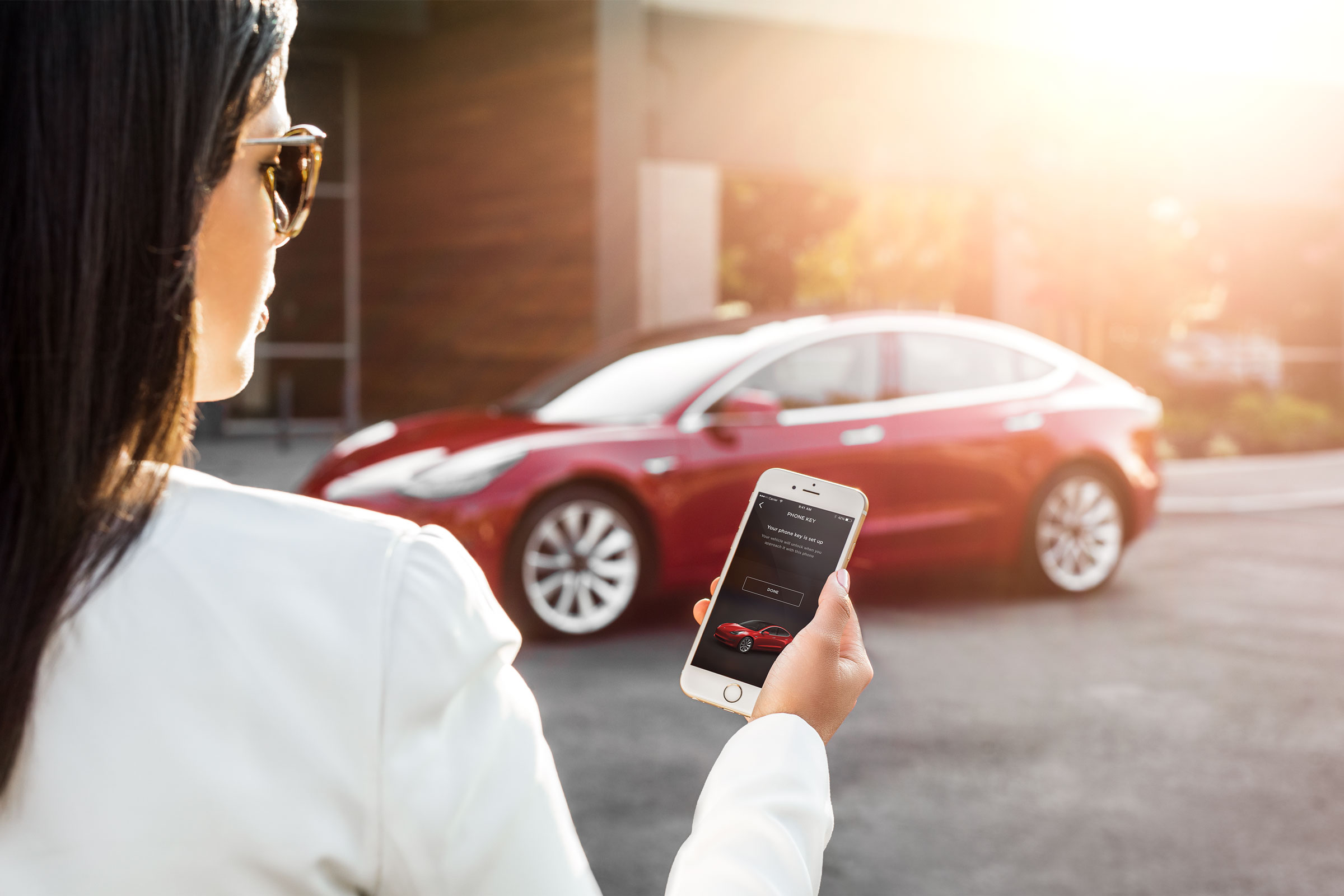 Woman looking at phone in front of a Tesla