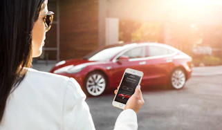 Woman looking at phone in front of a Tesla