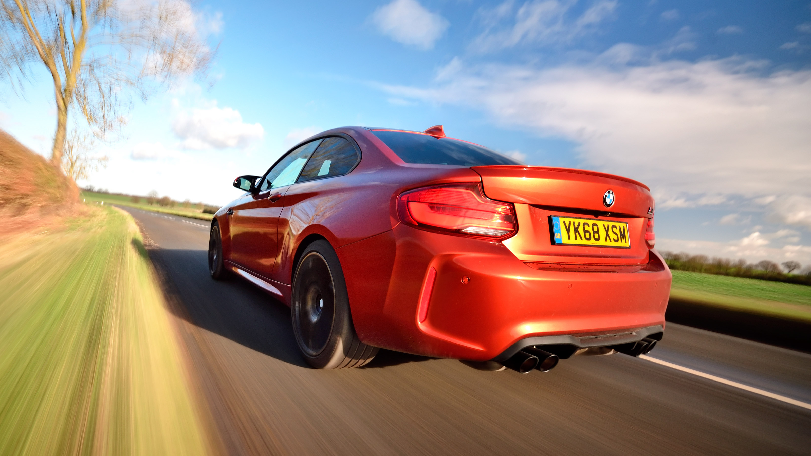 Orange BMW M2 driving - rear